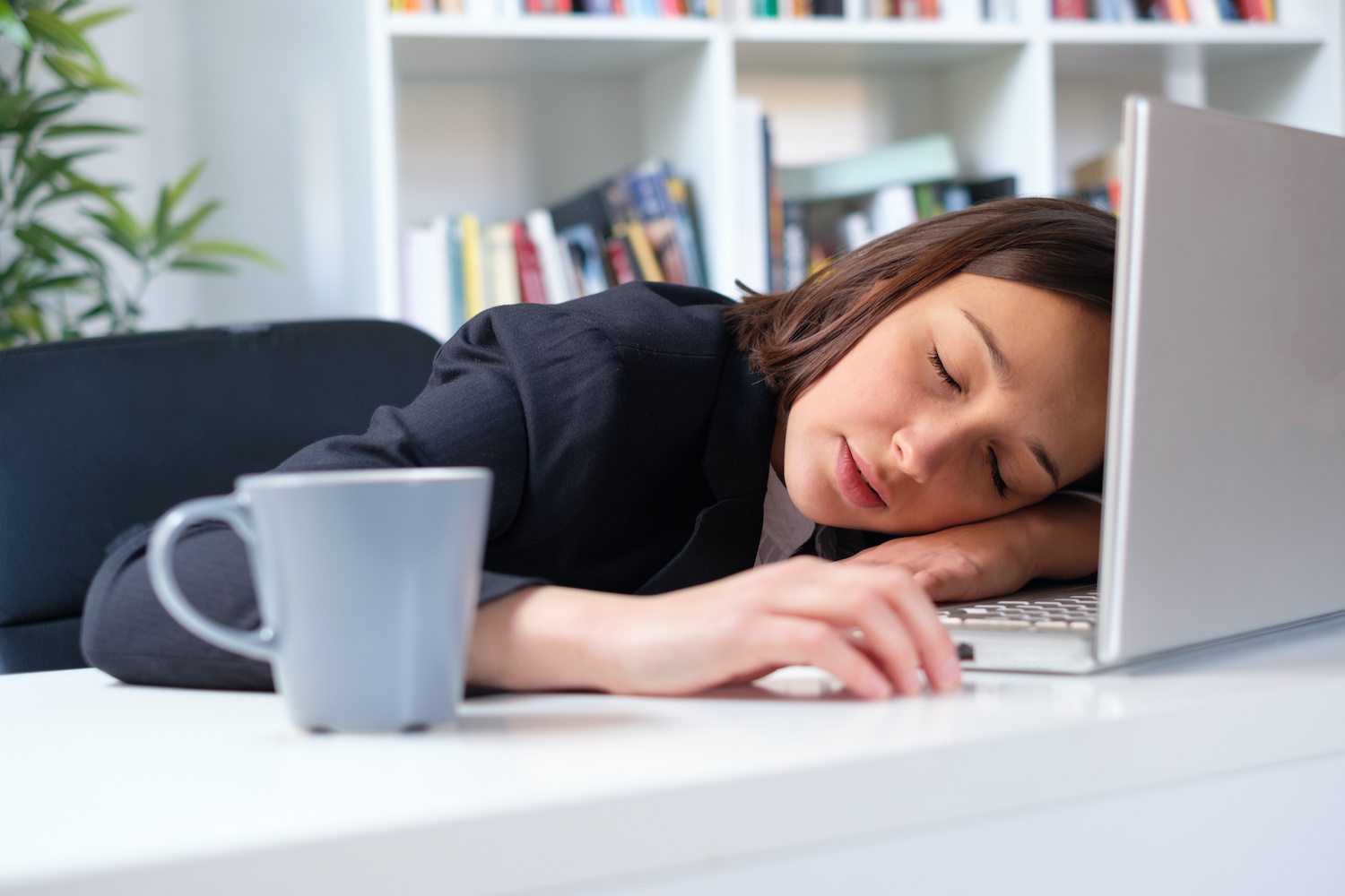 unproductive businesswoman asleep at her desk next to laptop and cup of coffee